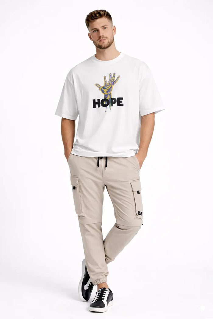 Model in Adrian carbon tan multi-pocket cargo pants with zip-off utility knees and white streetwear graphic tee.