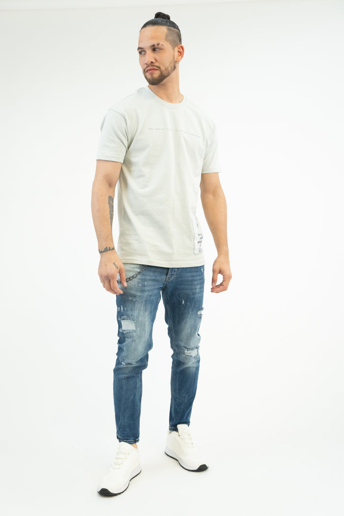 Men's Andy blue washed jeans featuring distressing and a metal pocket chain, styled with a grey tee and white sneakers.
