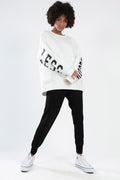 Model wearing the Ari white oversized sweatshirt with black sleeve lettering, black joggers, and white sneakers.