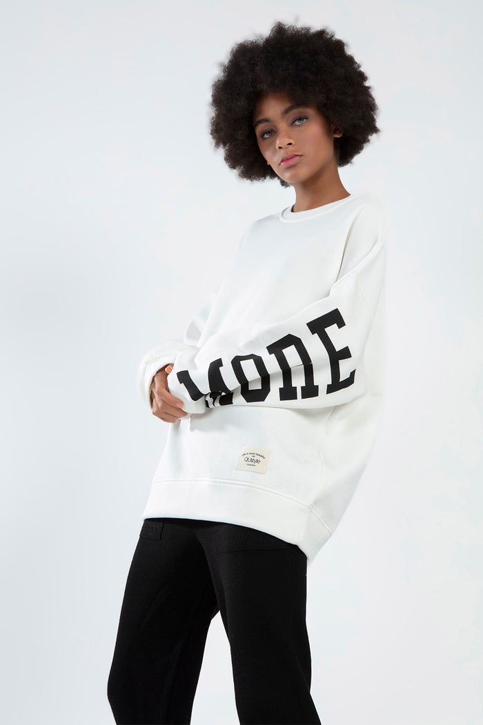 Model in white oversized Ari sweatshirt with black MODE graphic sleeve lettering and QUstyle patch.