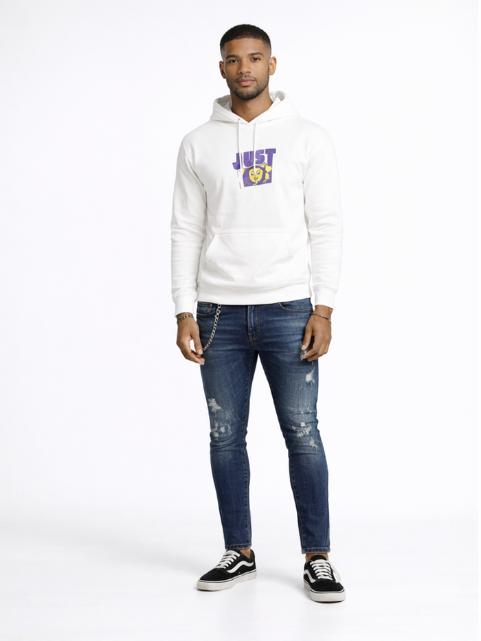 A man stands confidently in a white hoodie with a graphic design, paired with distressed blue jeans and black sneakers.