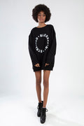Model in oversized black Blessed sweatshirt with streetwear circle graphic and black boots against white background.