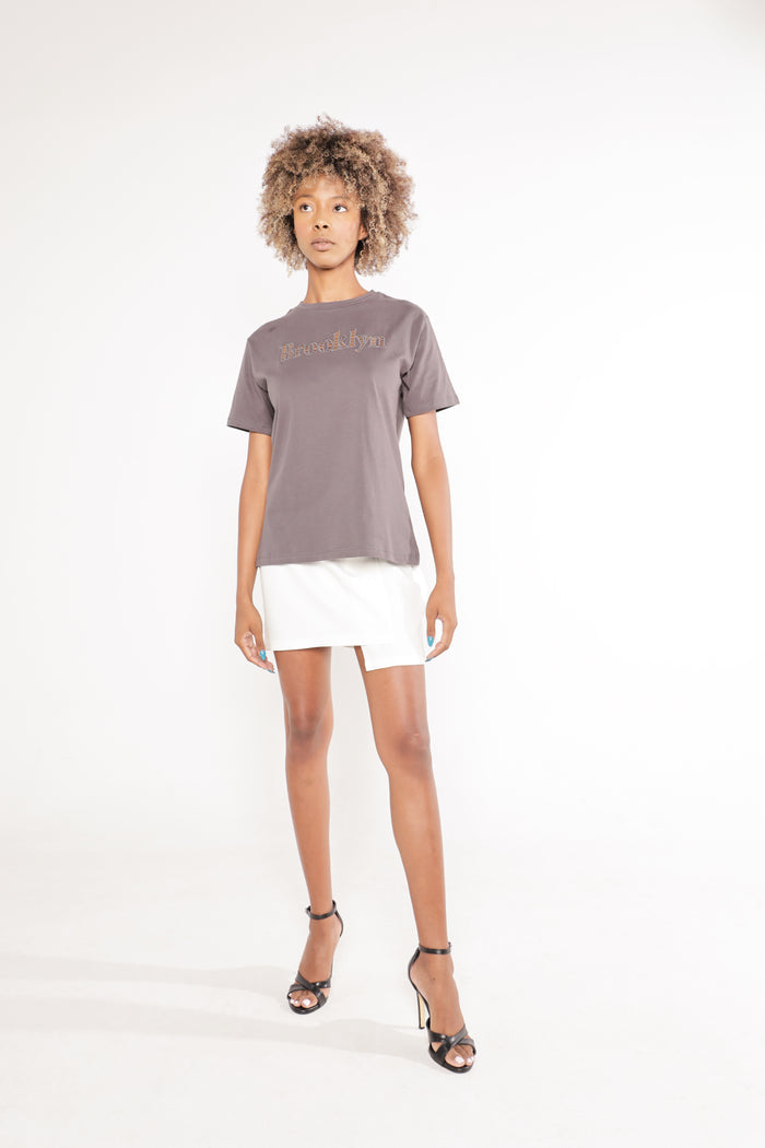 Model in a carbon gray Brooklyn graphic tee, white mini skirt, and black heels, showcasing an urban streetwear style.