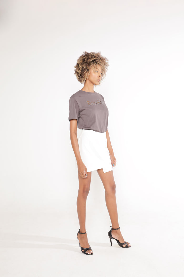 Model in Carbon gray Brooklyn graphic streetwear tee tucked into a white mini skirt with black heels.