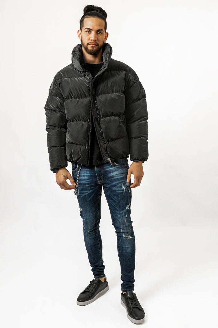 Man in Brooks black puffer coat with high collar, paired with distressed blue skinny jeans and black sneakers.