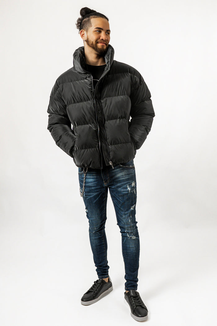 Man wearing Brooks black puffer coat with high collar, paired with distressed blue jeans and black sneakers.
