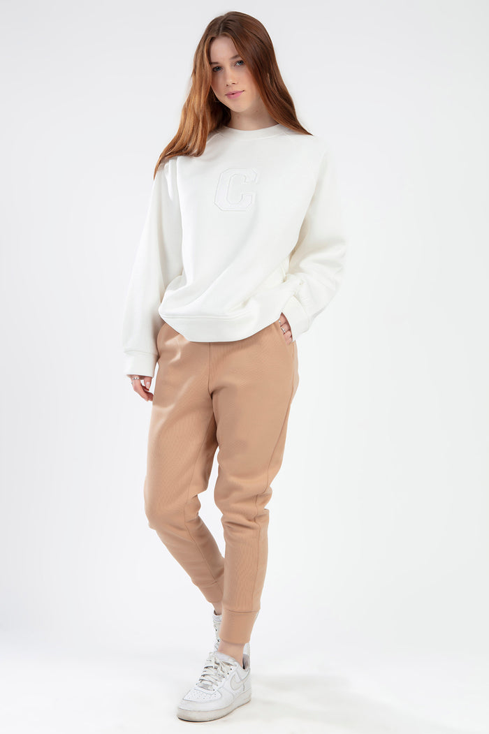 Model in a cream oversized crewneck sweatshirt with embossed C logo and tan ribbed joggers.