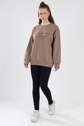 Brown oversized San Francisco California embroidered sweatshirt worn with black leggings and white sneakers.