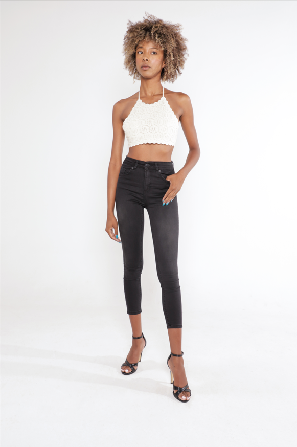 Model wearing a Carbon Knit cream halter crop top and black high-waisted skinny jeans with heels.