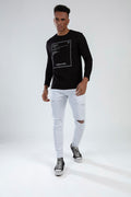 Model wearing Carlos white slim fit distressed jeans with knee rips and a black Carbon long sleeve streetwear tee.