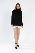Model wearing a Celine black oversized turtleneck knit sweater with a distressed fringe hem and white mini skirt.