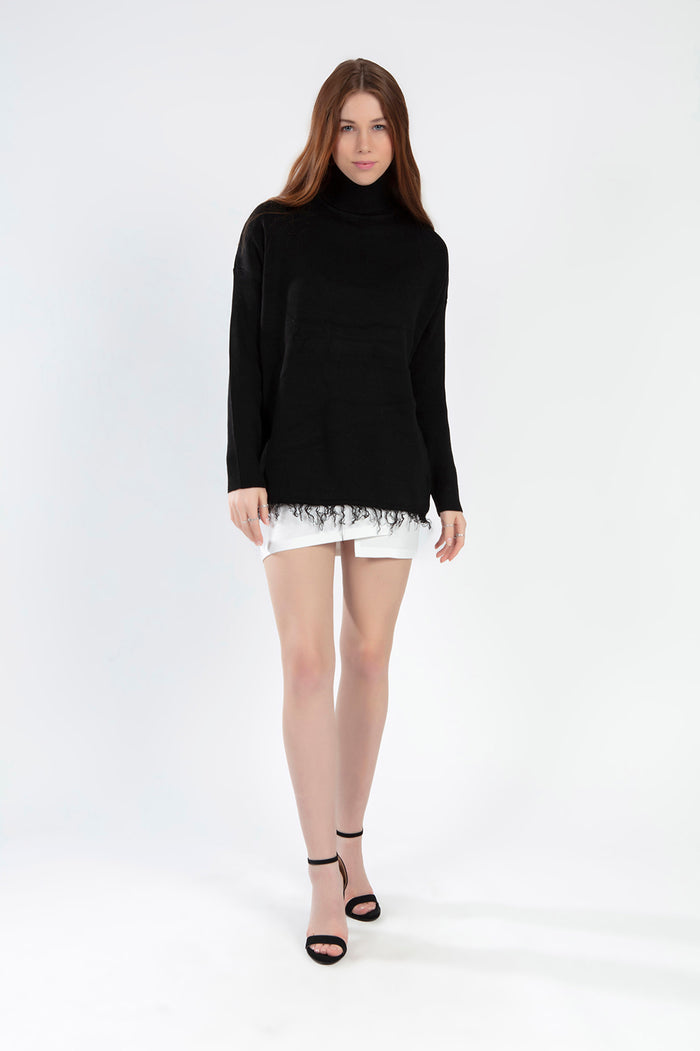 Model wearing a Celine black oversized turtleneck knit sweater with a distressed fringe hem and white mini skirt.