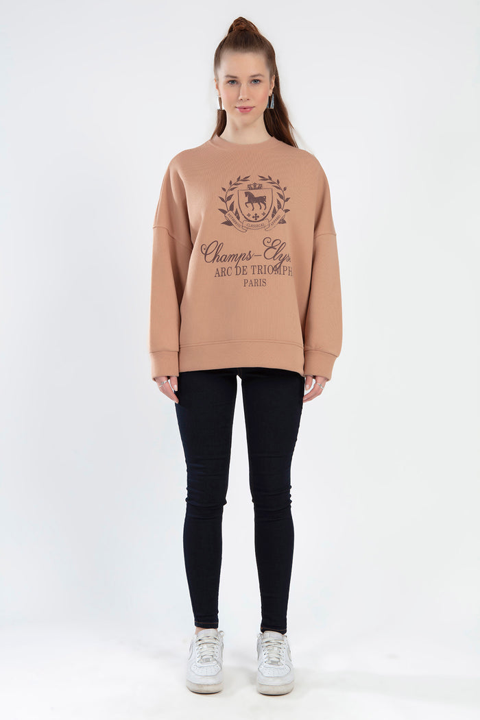 Model wearing Champs-Élysées brown oversized sweatshirt with graphic crest, black skinny jeans, and white sneakers.