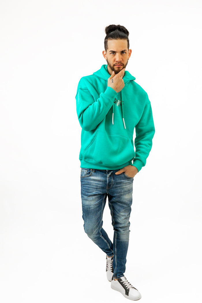Model wearing a Charles mint green oversized hoodie and slim blue jeans in a professional studio streetwear style.