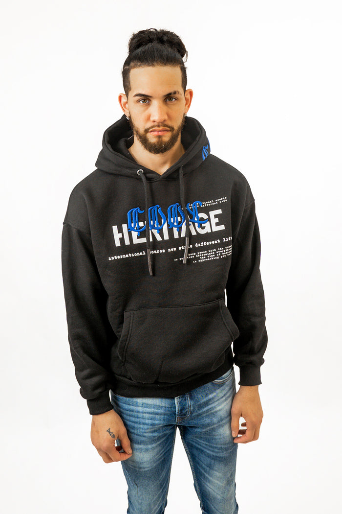 Man in a black Carbon Jeans Heritage oversized hoodie with blue embroidery, streetwear style on white background.