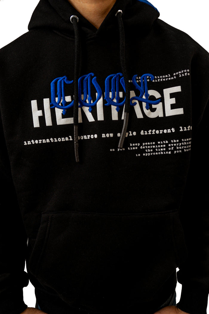 Close-up of black streetwear hoodie with blue and white Heritage embroidery and graphic typography.