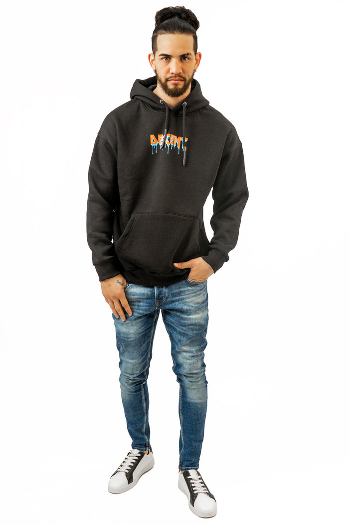 Man wearing the Decent black streetwear hoodie with orange graffiti logo and blue distressed jeans.