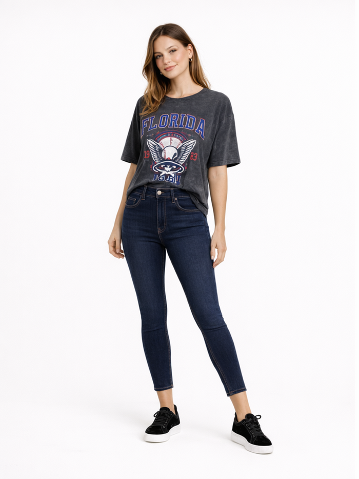 A woman poses in a gray graphic tee featuring a baseball design, paired with dark skinny jeans and black sneakers.