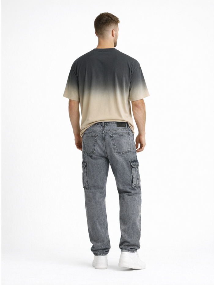A man stands with his back to the camera, wearing gray cargo jeans and a gradient t-shirt.