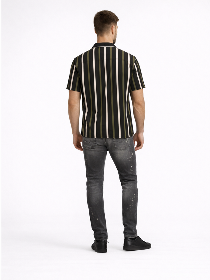 A man stands with his back to the camera, wearing a short-sleeve striped shirt and distressed jeans.