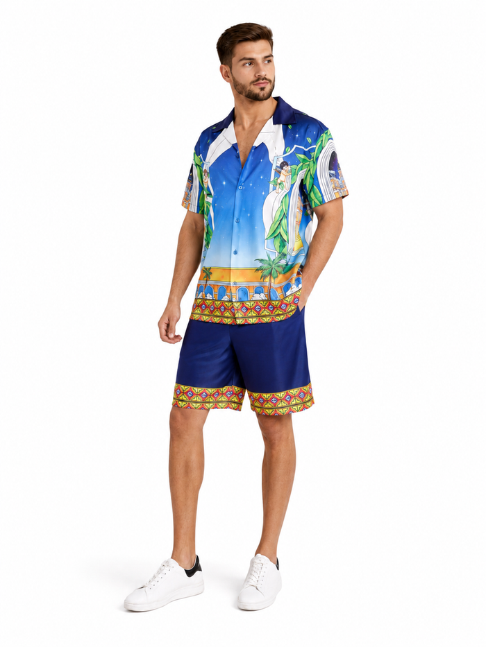 A man stands wearing a colorful short-sleeve shirt with tropical designs and matching shorts, paired with white sneak...