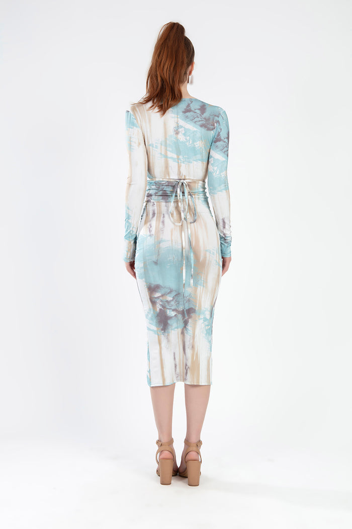 A woman wearing a long-sleeve, tie-dye dress with a fitted silhouette and open back, paired with block-heeled sandals.