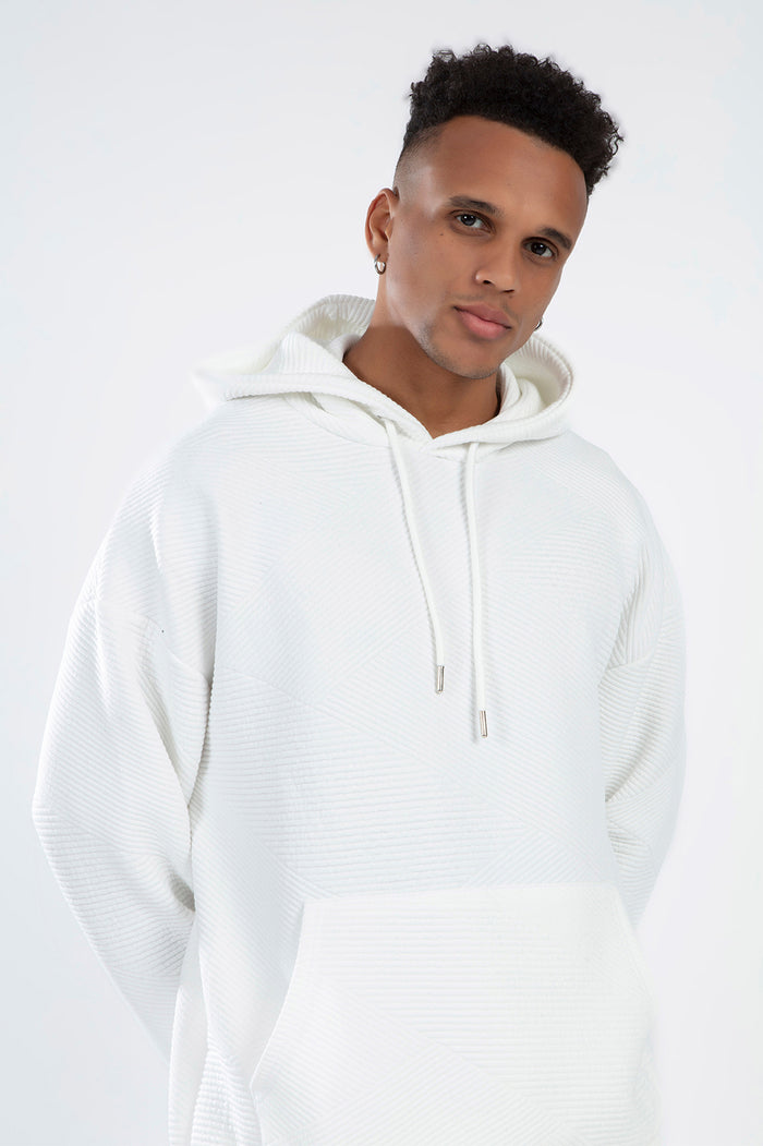 Man in white Eric Eric Hoodie showing diagonal ribbed knit texture, front pocket, and adjustable drawstrings streetwear.