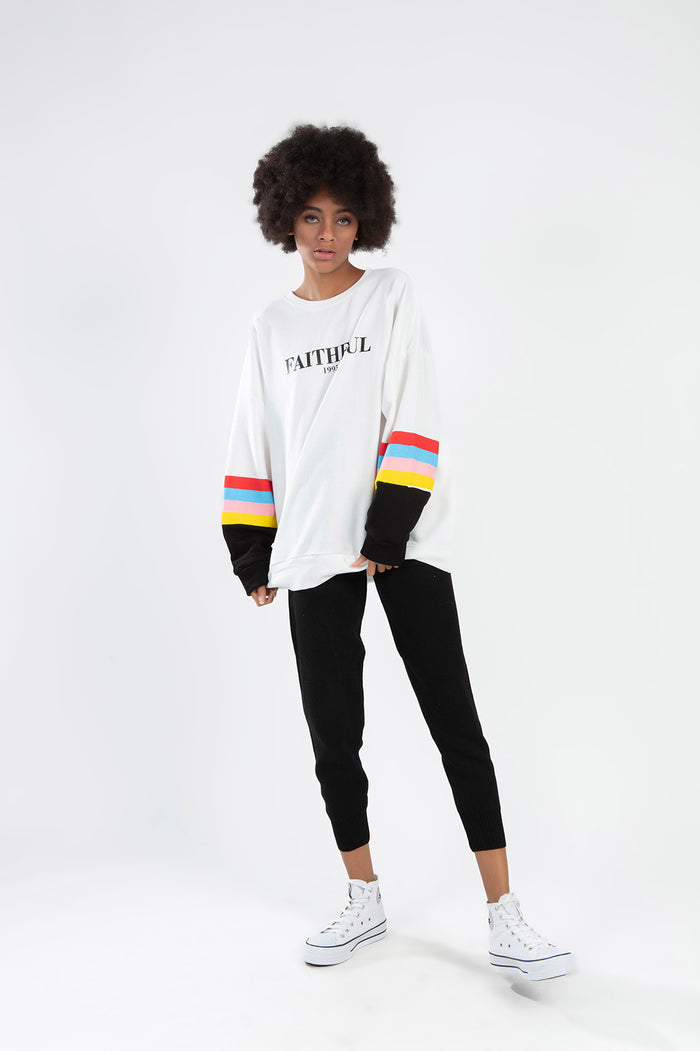 Model in White Faithful 1995 Oversized Long Sleeve Top with Colorful Striped Sleeves and Black Joggers.