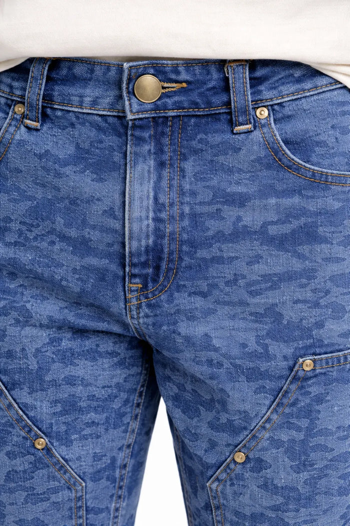 Close-up of blue patterned denim jeans featuring a button closure and angled pockets with decorative stitching.