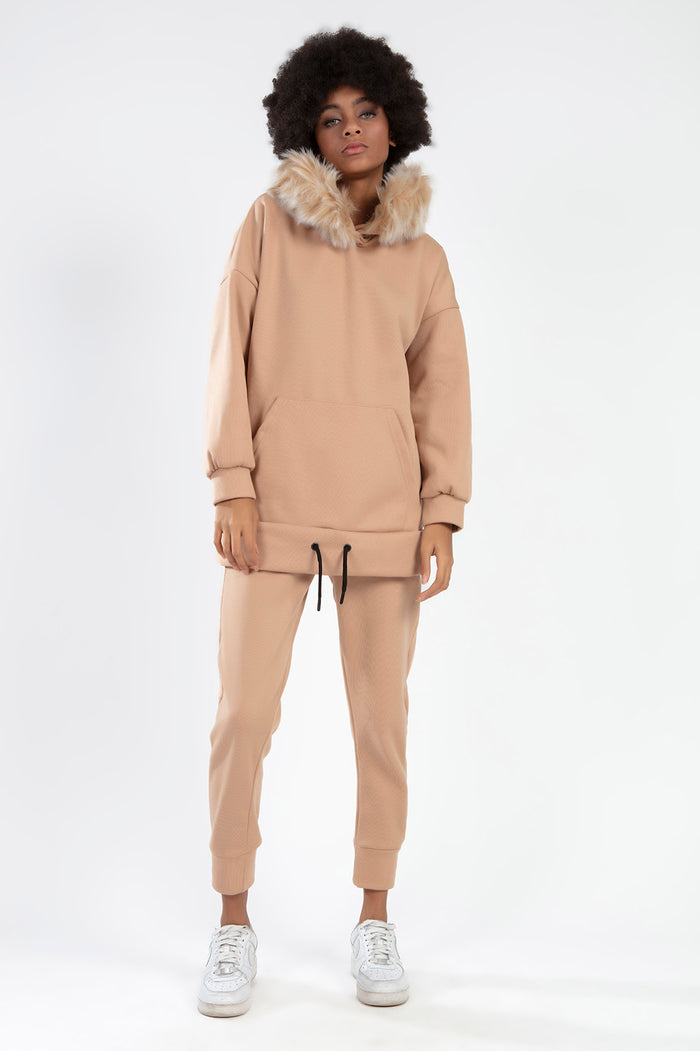 Model in a tan textured two-piece set featuring a furry faux fur trim hood, oversized hoodie, and matching joggers.