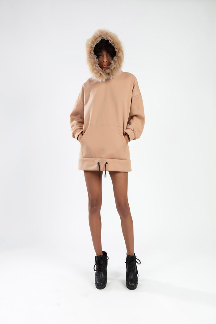 Model wearing an oversized tan hoodie with a faux fur-trimmed hood and front pocket, styled as a trendy streetwear top.