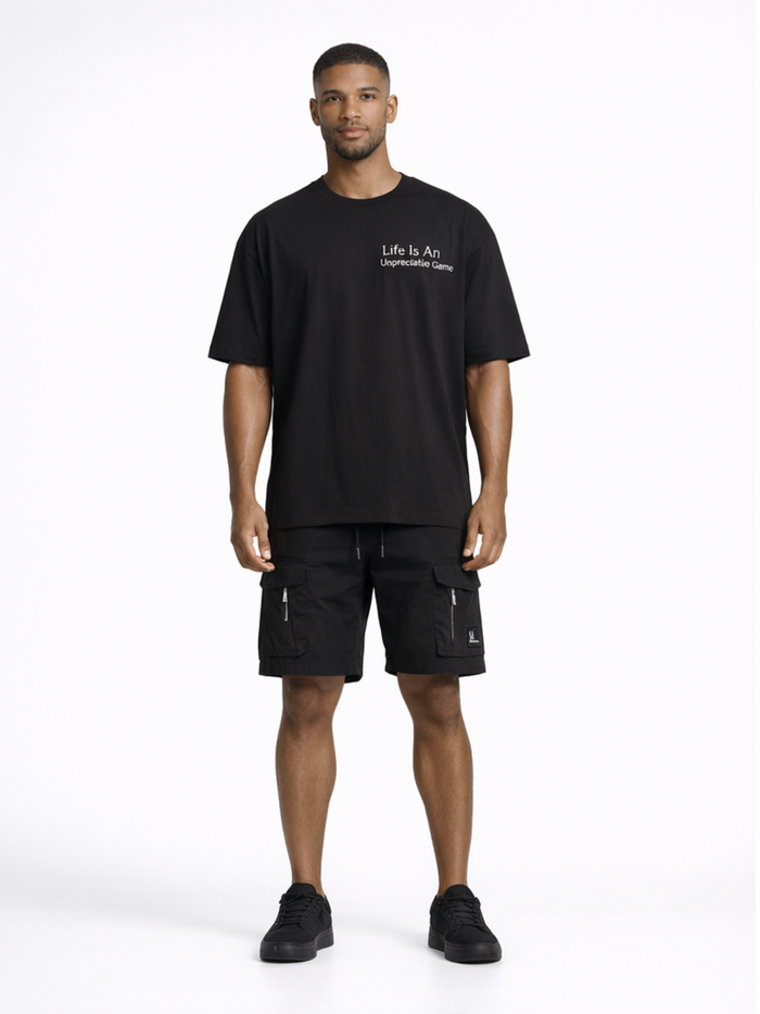 A man stands confidently in a black oversized t-shirt paired with cargo shorts and sneakers.