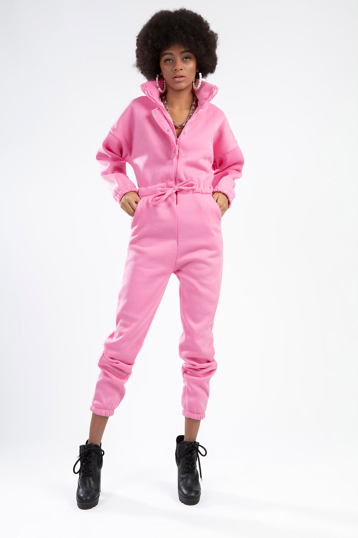 Model wearing the Gem Romper, a pink long-sleeve jumpsuit with a high collar, drawstring waist, and pockets.