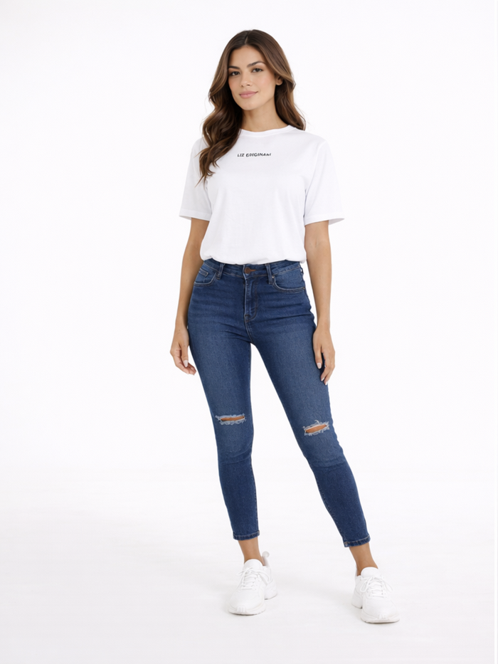 A woman stands confidently in a casual white t-shirt and fitted blue jeans with distressed details.