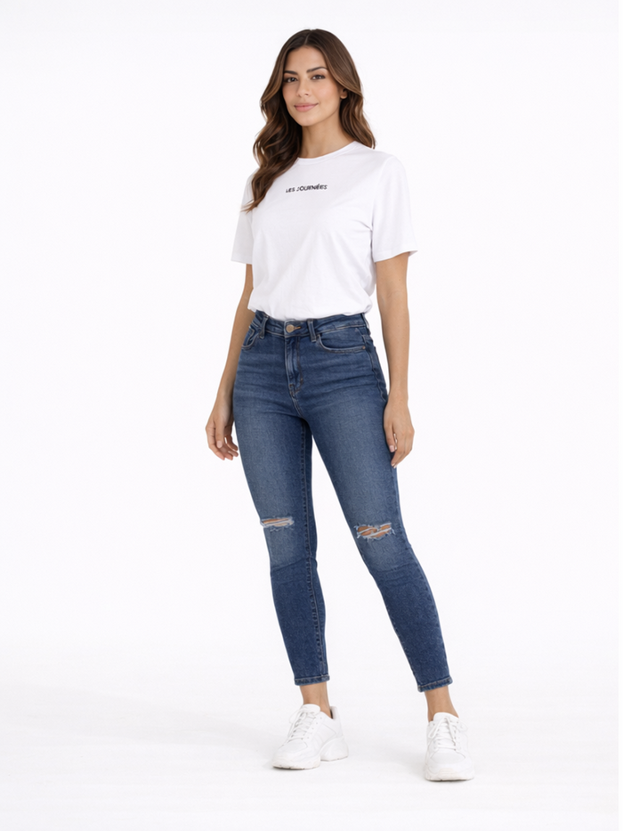 A woman stands confidently in a casual white t-shirt and distressed blue jeans, paired with white sneakers.