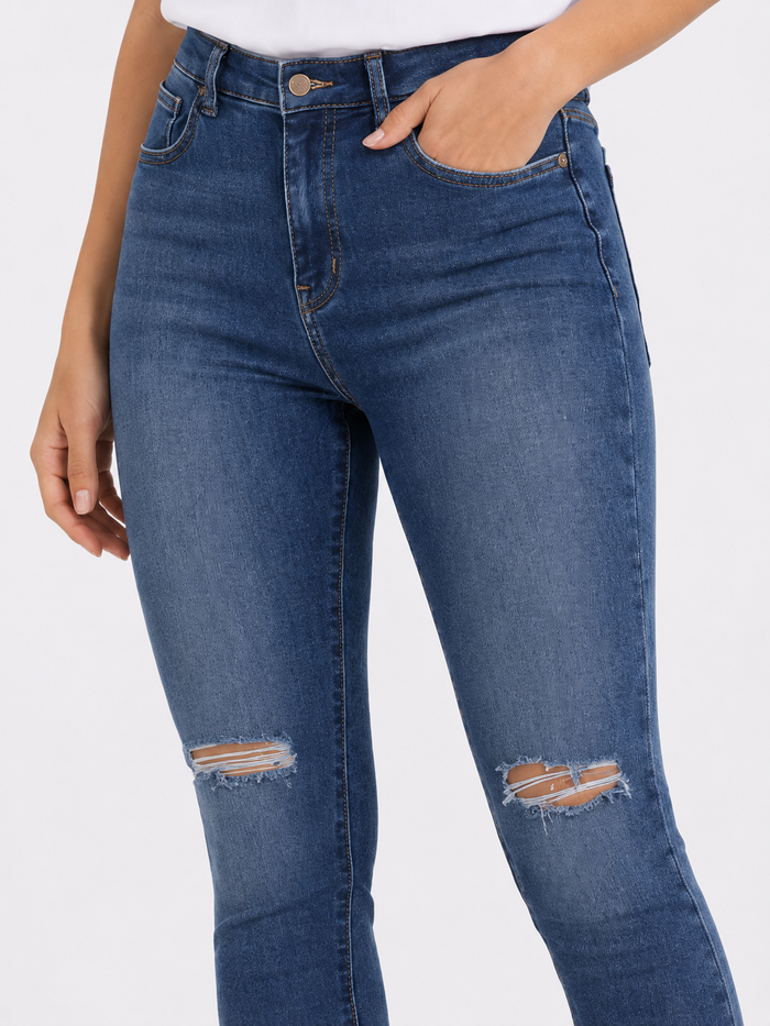 Close-up of a person wearing dark blue ripped jeans with a high waist and a hand in the pocket.