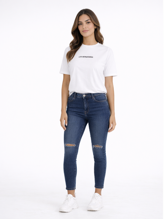 A woman stands confidently in a white t-shirt and distressed blue jeans, paired with white sneakers.