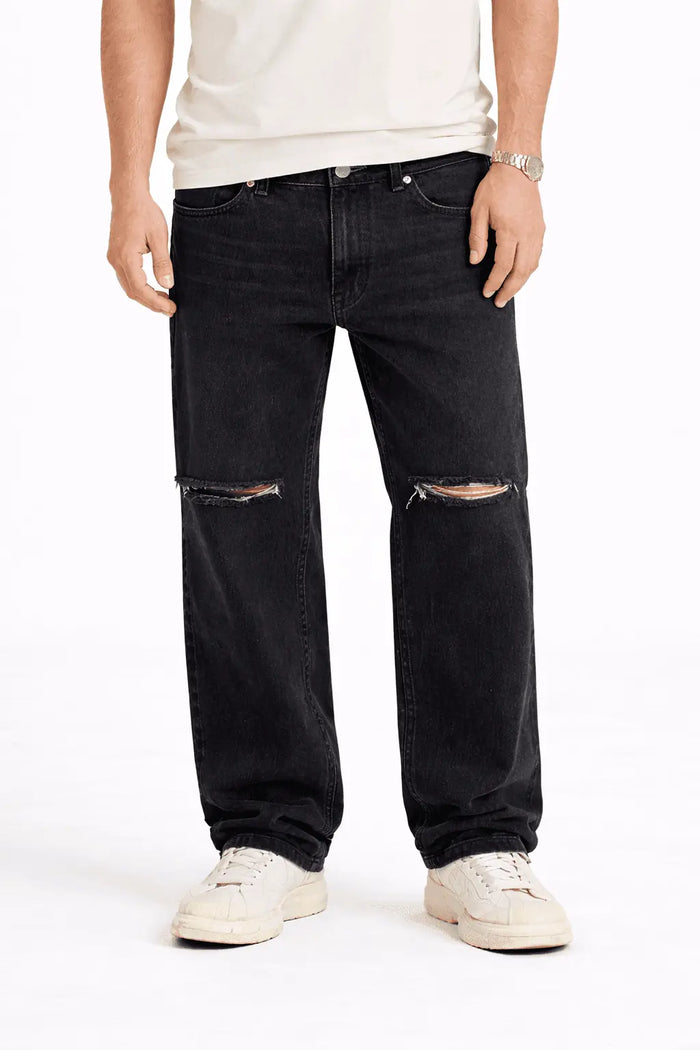 Model wearing Carbon black baggy fit denim jeans with distressed knee rips and streetwear aesthetic.