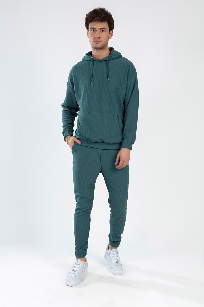 Man wearing the Gordon Two-Piece Pants Set in Carbon turquoise ribbed fabric with a hooded sweatshirt and joggers.