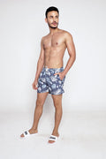 Model wearing Hank Swimwear blue floral patterned swim trunks with white drawstrings and Carbon Jeans slides.