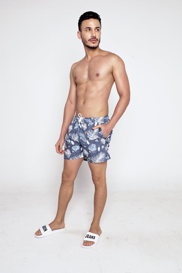 Model wearing Hank Swimwear blue floral patterned swim trunks with white drawstrings and Carbon Jeans slides.