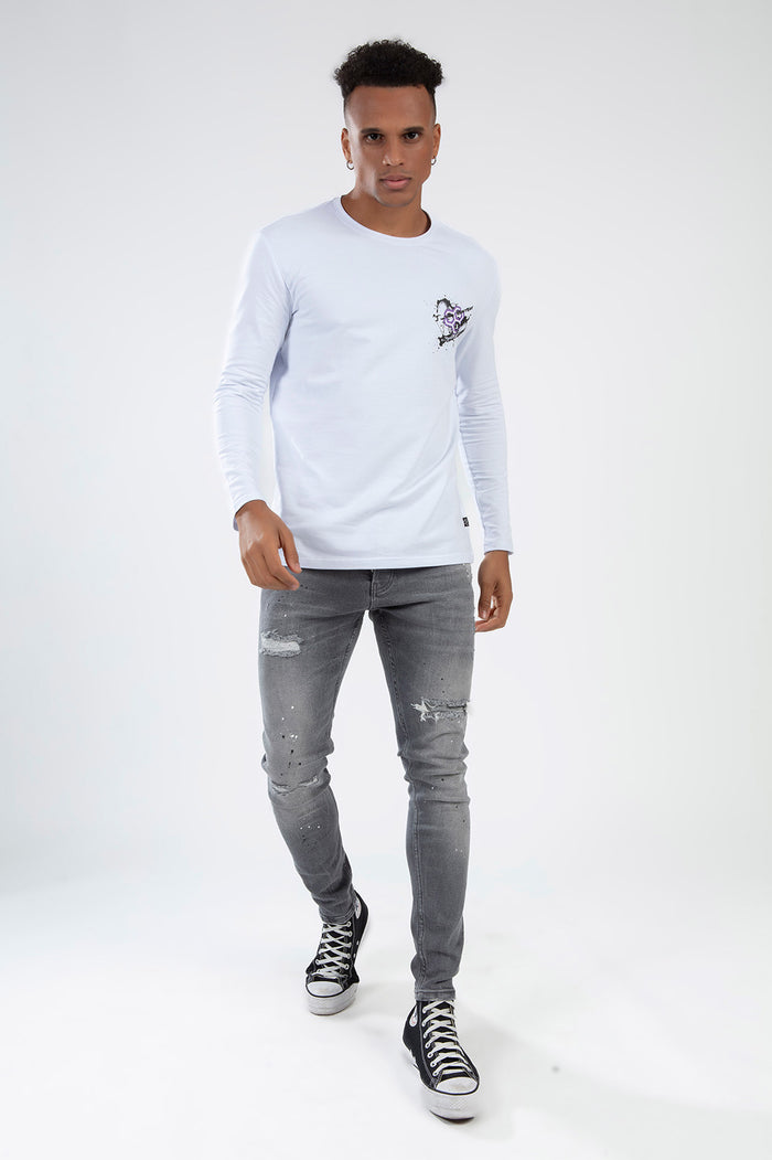 Man in a white Heartbit long sleeve graphic t-shirt and distressed gray skinny jeans for streetwear style.