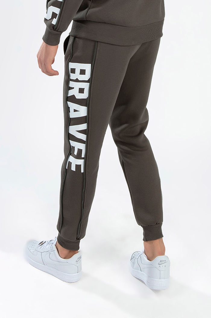 Army Green Ian Pants Set by Carbon Jeans, featuring side-leg BRAVEE logo with zipper detail and relaxed jogger fit.