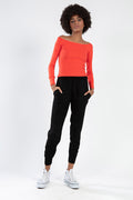 Model in a red off-the-shoulder long sleeve top paired with black joggers and white high-top sneakers.