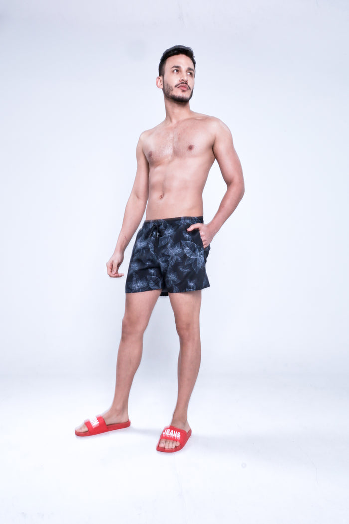 Man modeling Jaxon floral patterned swim trunks in black with red slides, showcasing trendy men's summer swimwear style.
