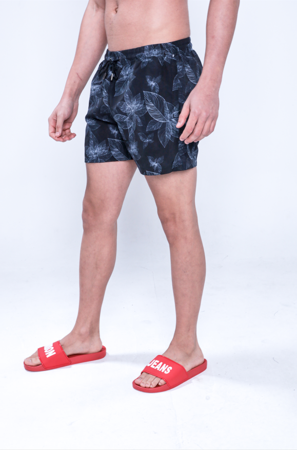 Jaxon men's black floral swim trunks with white leaf patterns and red logo slides, side view.