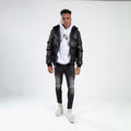 Man in Jerry Puffer Coat, a black insulated jacket with faux fur collar, over a white hoodie and distressed jeans.
