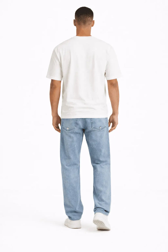 A person wearing a white t-shirt and light blue jeans stands with their back to the camera.