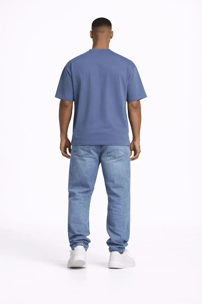 A person stands with their back to the camera, wearing a blue shirt and light blue jeans, paired with white sneakers.
