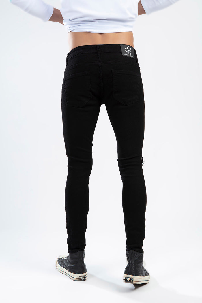 A person wearing fitted black jeans and black high-top sneakers, viewed from the back against a plain background.
